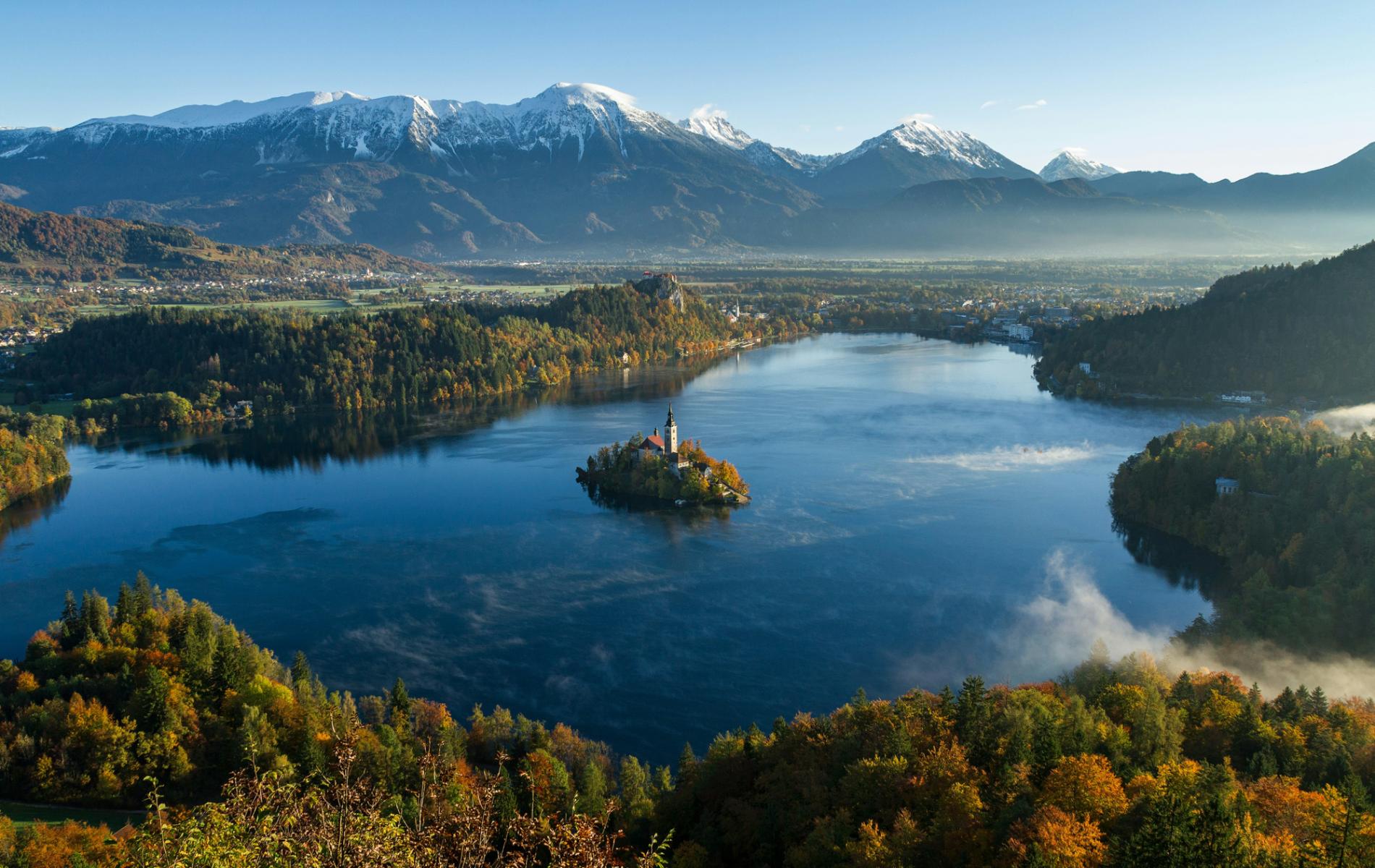 Der malerische Bleder See in Slowenien mit einer Insel in der Mitte, umgeben von herbstlich gef&auml;rbten W&auml;ldern und imposanten Bergen im Hintergrund