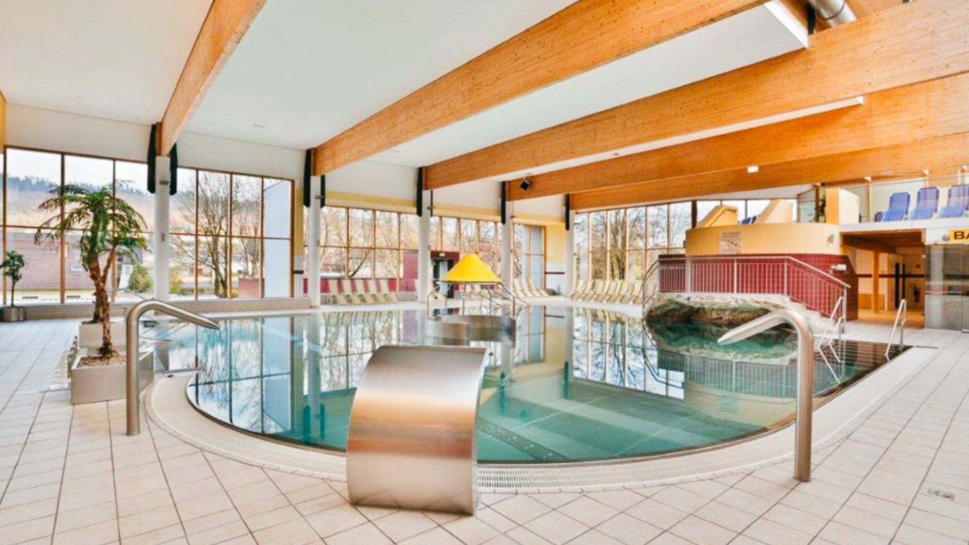 Innenpoolbereich des Sporthotel Kapfenberg mit großer Glasfront, Wasserfall-Element und Liegebereich