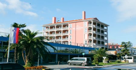 Au&szlig;enansicht des Hotels Aquapark Zusterna mit rosa Fassade, Balkonen und der slowenischen Flagge.