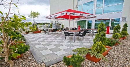 Ein modernes Hotelgeb&auml;ude mit auff&auml;lligen geometrischen Mustern in Braun und Wei&szlig;, umgeben von gr&uuml;nen B&auml;umen und einem gro&szlig;en Parkplatz im Vordergrund.