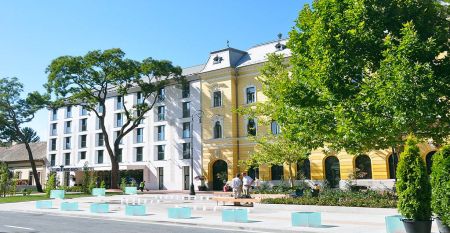 Außenansicht des Hotels Gingko mit einer modernen Fassade und einem historischen Flügel, umgeben von grünen Bäumen und einem gepflegten Platz.