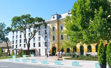 Außenansicht des Hotels Gingko mit einer modernen Fassade und einem historischen Flügel, umgeben von grünen Bäumen und einem gepflegten Platz.