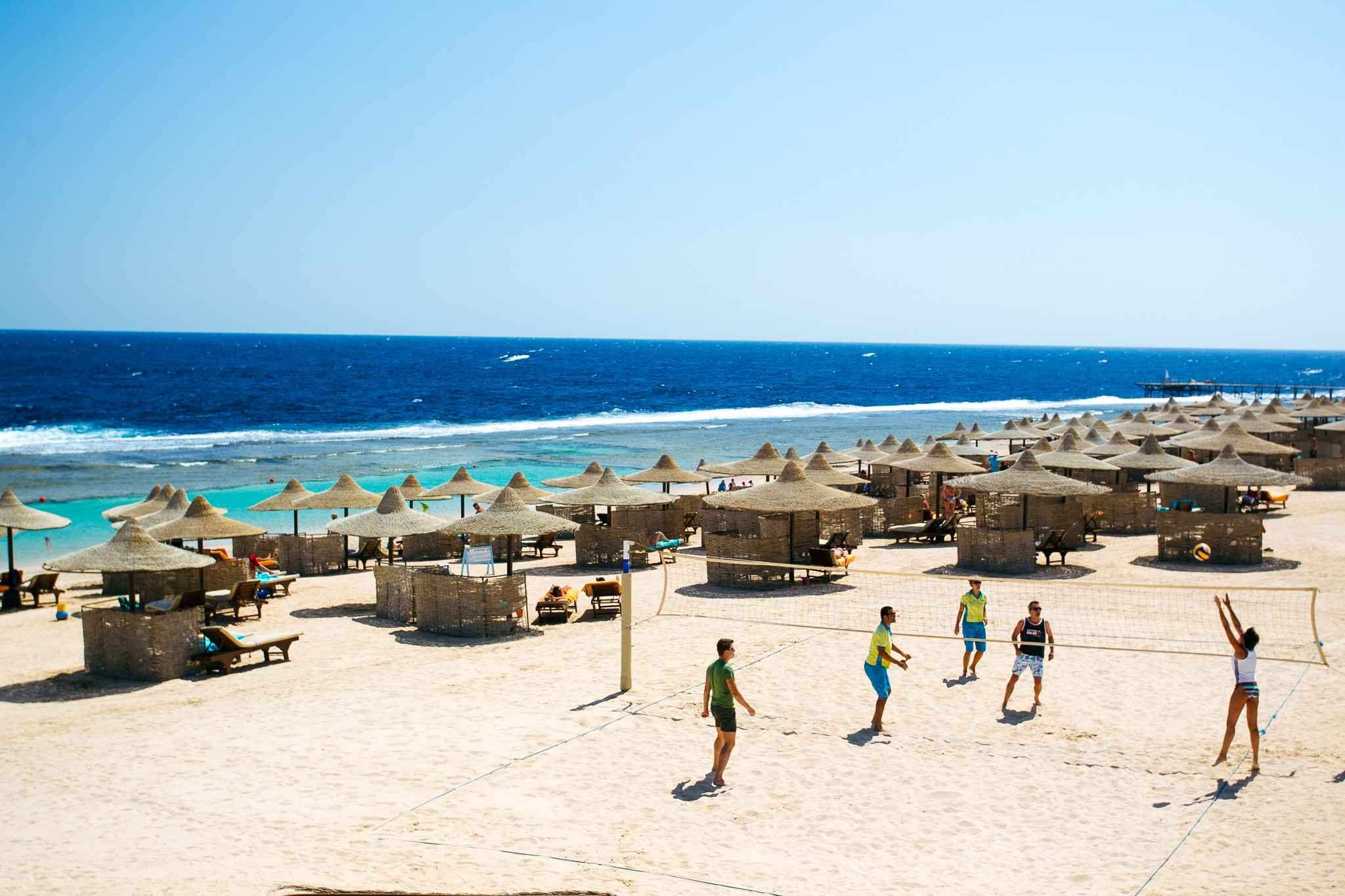 Strand in &Auml;gypten mit Volleyballspielern, Sonnenschirmen und dem klaren blauen Meer im Hintergrund.