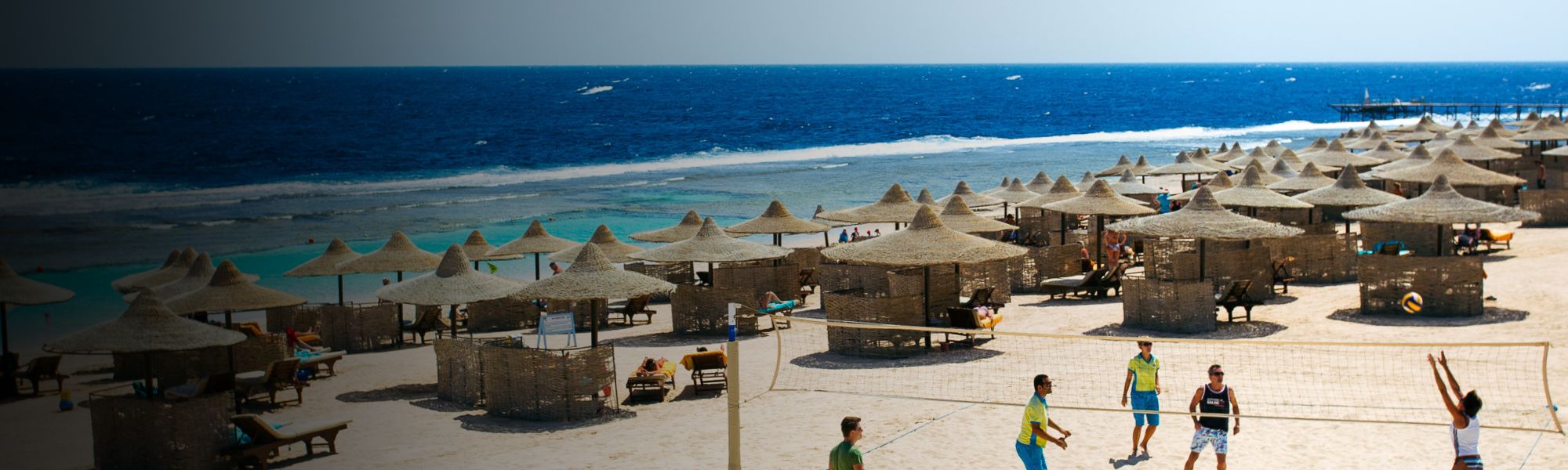 Beachvolleyball-Spiel am Strand in &Auml;gypten mit Sonnenschirmen und dem blauen Meer im Hintergrund.
