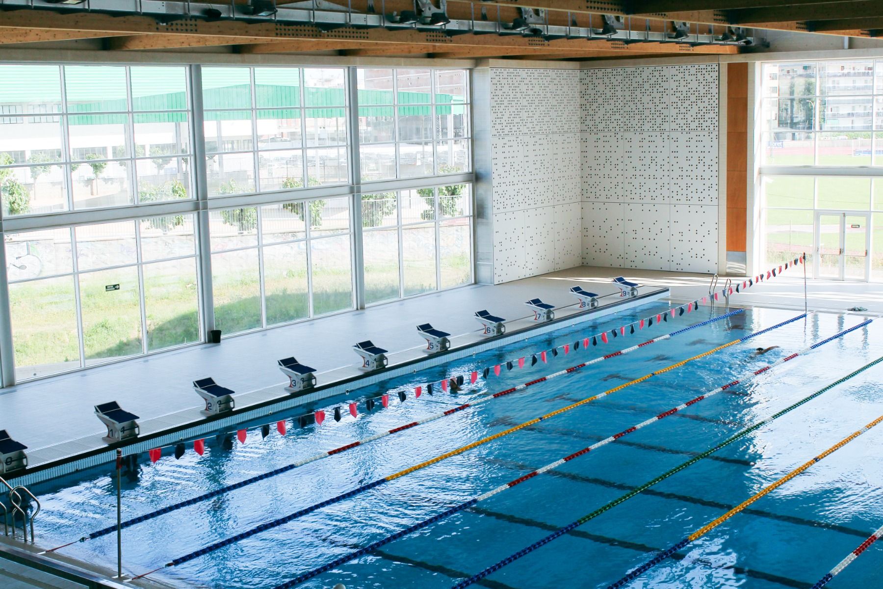 Modernes Hallenbad mit Wettkampfbahnen, Startblöcken und großen Glasfenstern, die für viel Tageslicht sorgen.