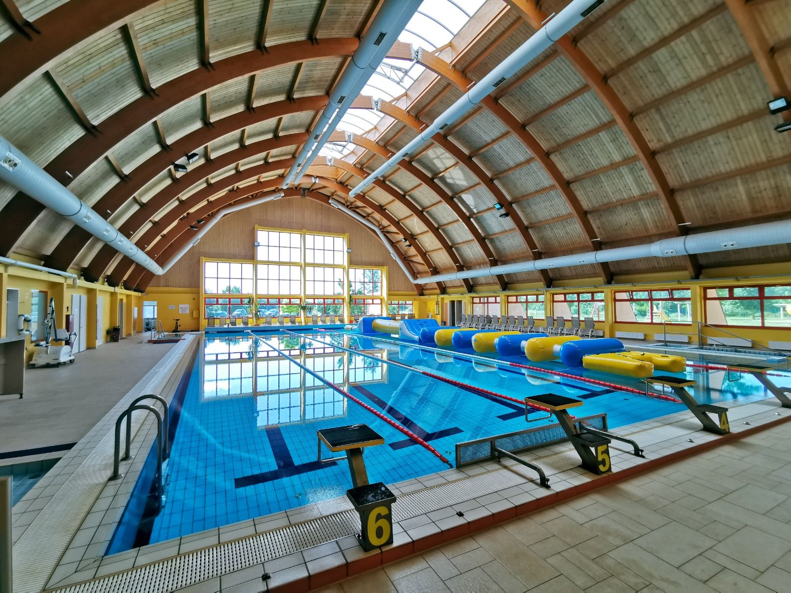 Ein großes Hallenbad mit einer gewölbten Holzdecke und verschiedenen Schwimmbahnen, ideal für Trainingslager.