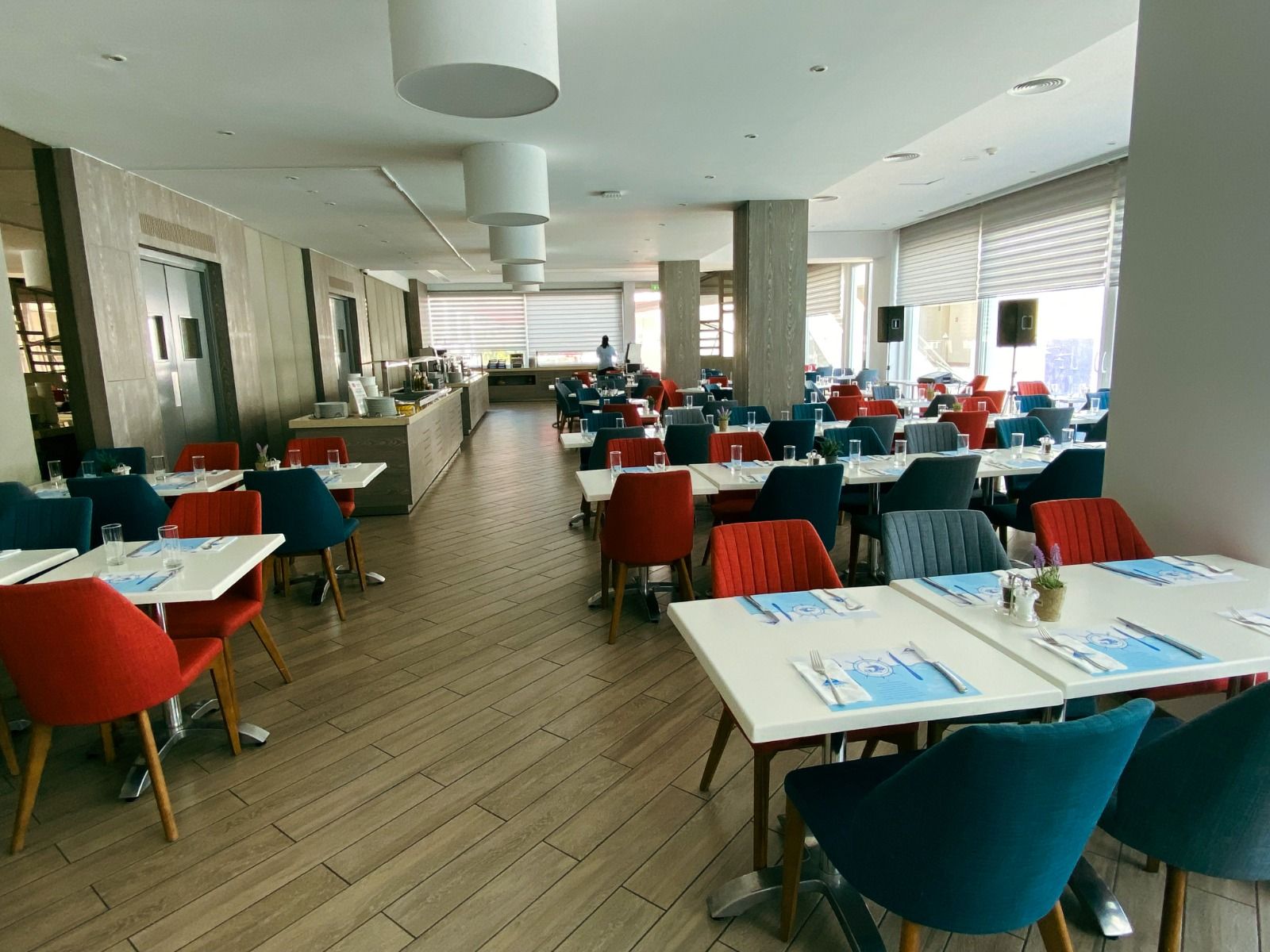 Gemütliches Restaurant mit grünen und roten Stühlen mit einer großen Fensterfront.