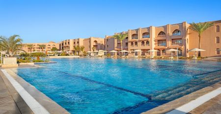 Aqua Vista Resort offers multiple outdoor pools, sun loungers, and umbrellas beneath clear blue skies&mdash;perfect for ein erfolgreiches Trainingslager in den Wintermonaten&mdash;with buildings and the sea in the background.
