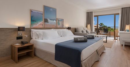 Modernes Hotelgeb&auml;ude bei Nacht mit beleuchtetem Eingang und Kakteen im Vordergrund.