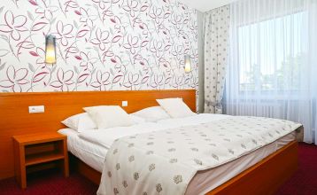 Ein modernes Hotelgebäude mit auffälligen geometrischen Mustern in Braun und Weiß, umgeben von grünen Bäumen und einem großen Parkplatz im Vordergrund.