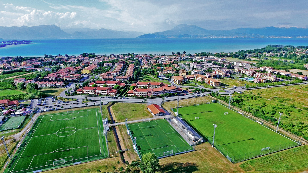 Fu&szlig;ballpl&auml;tze inmitten einer mediterranen Stadtlandschaft mit Blick auf einen blauen See und umliegende Berge.