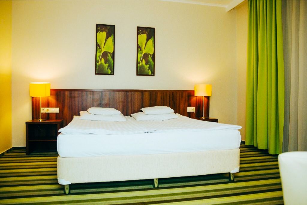 Stilvolles Hotelzimmer im Gingko Hotel mit einem großen Doppelbett, grünen Vorhängen und warmer Beleuchtung.