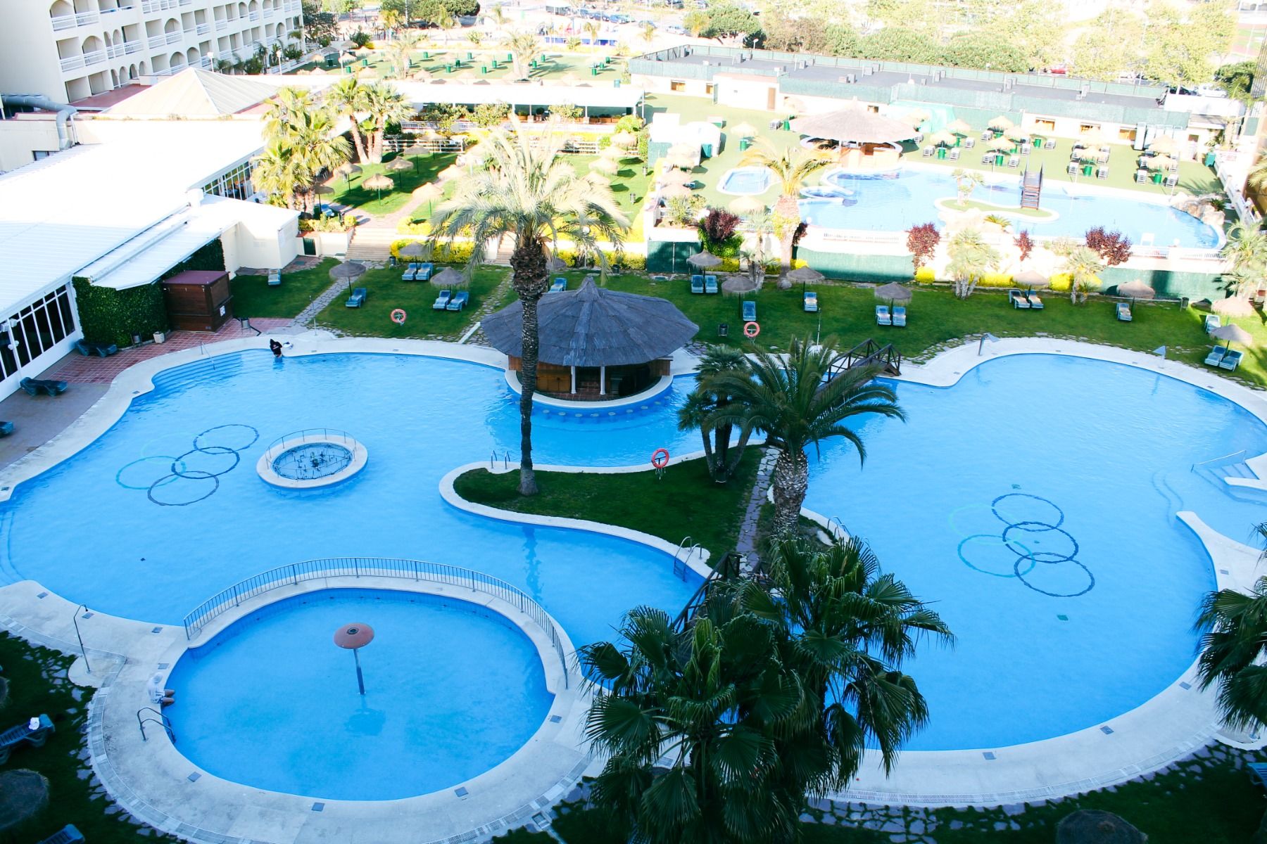 Große Poollandschaft mit verschiedenen Schwimmbecken, Palmen und Liegebereich im Außenbereich des Hotels.