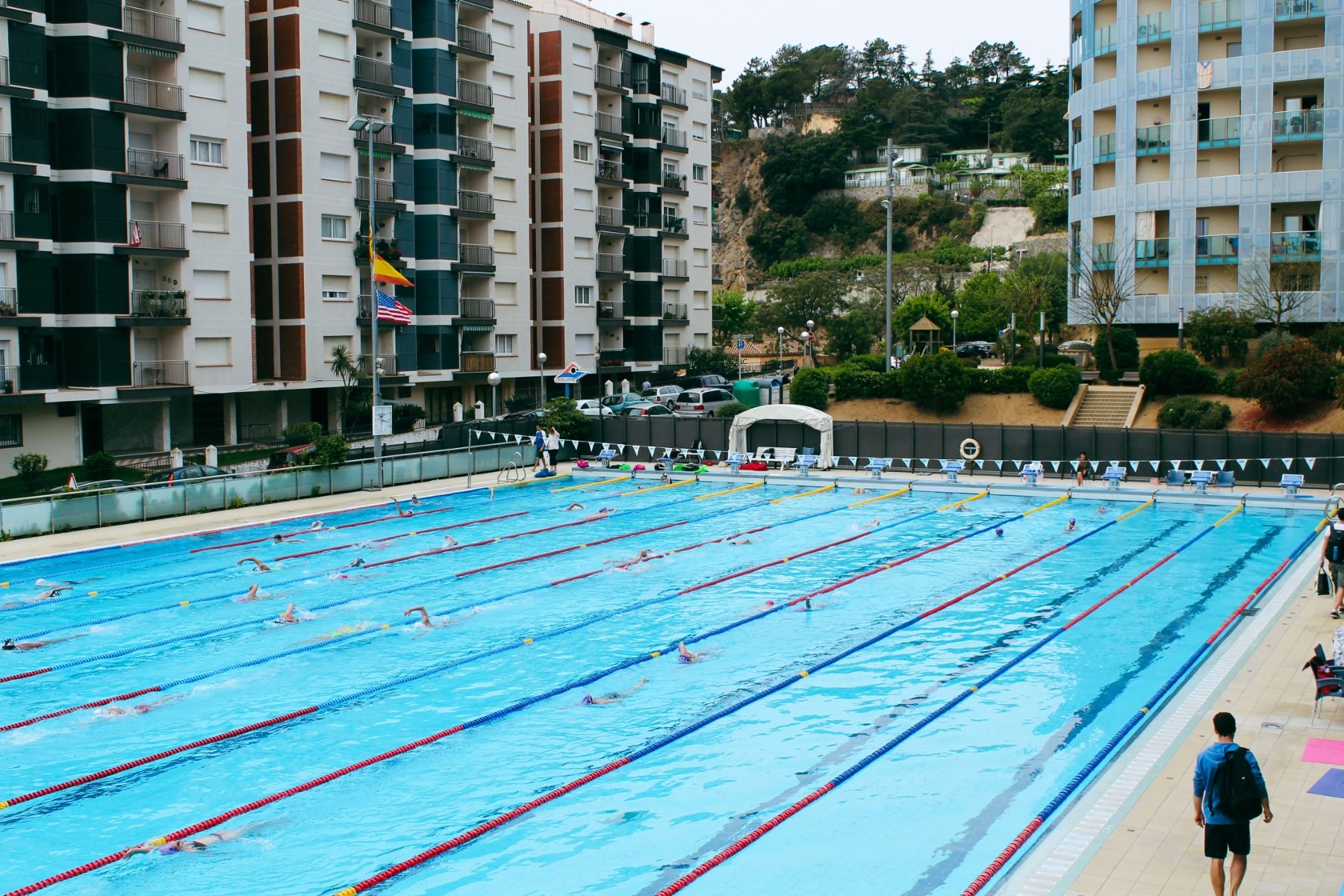 Großes Schwimmbecken für Training mit mehreren Bahnen, umgeben von Wohngebäuden und grüner Landschaft.