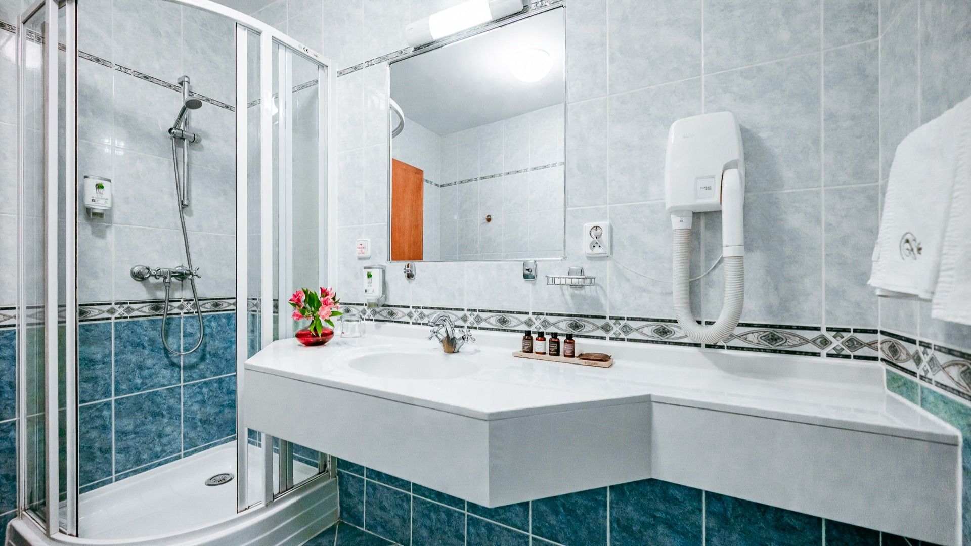 Modern ausgestattetes Badezimmer mit Dusche, großem Spiegel, hellen Fliesen und Pflegeprodukten.