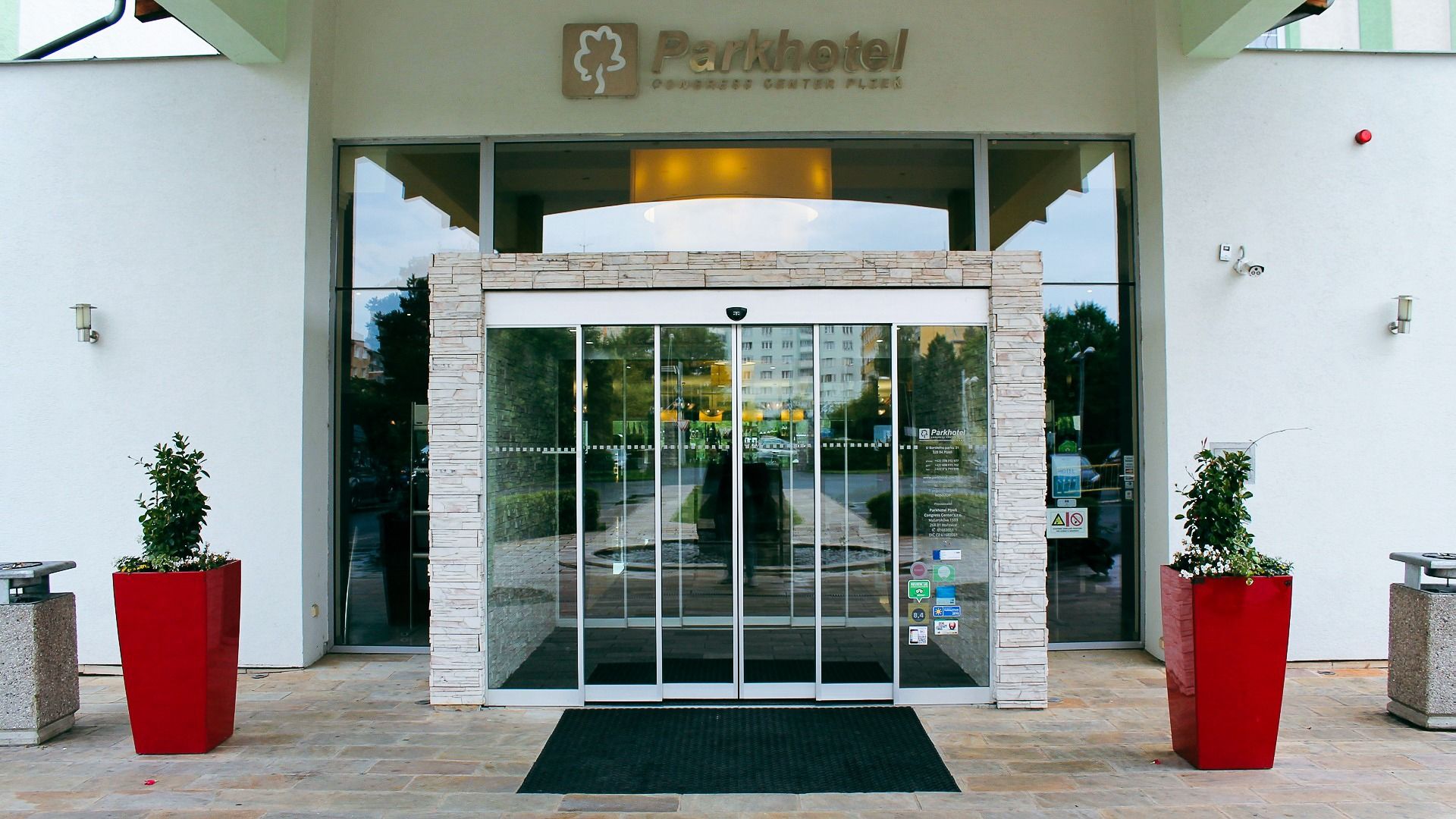 Hotelhaupteingang mit automatischen Glastüren und dekorativen roten Blumentöpfen.