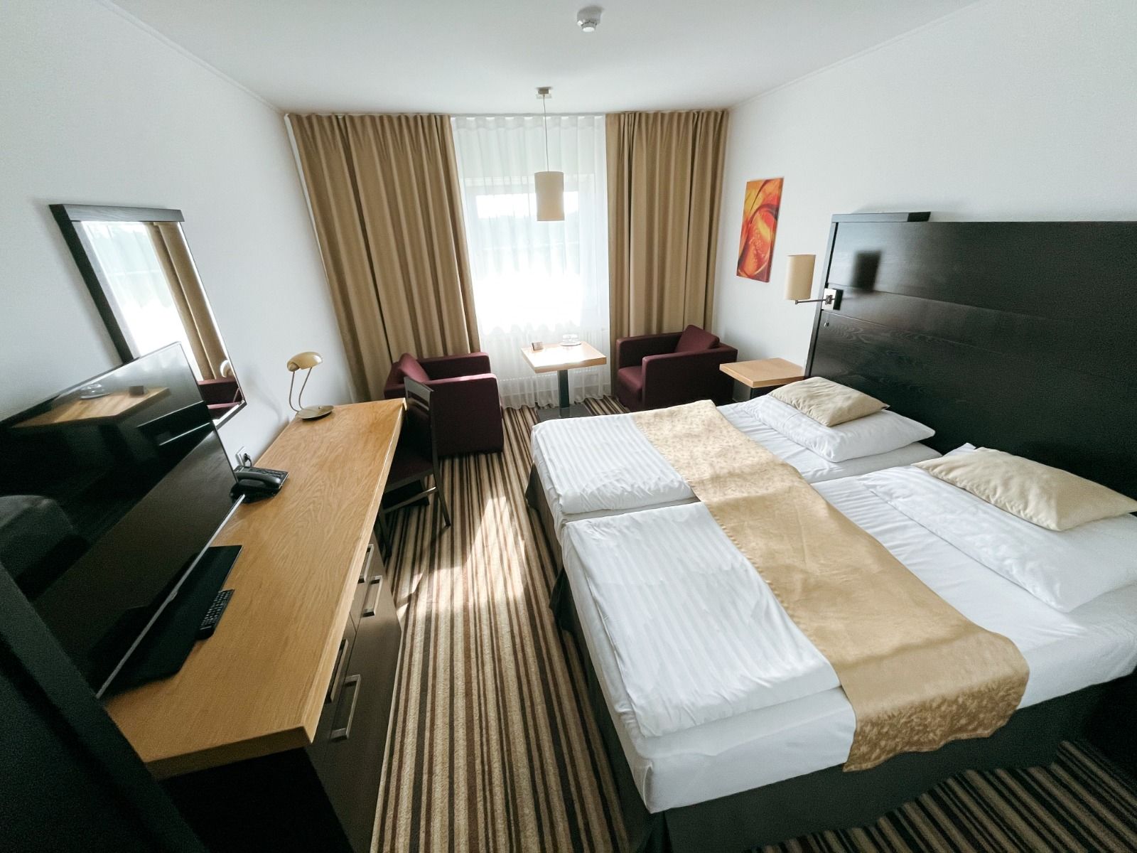 Innenaufnahme eines Zimmers mit Doppelbett, dunklem Holzdekor und kleinem Tisch mit zwei Sesseln.