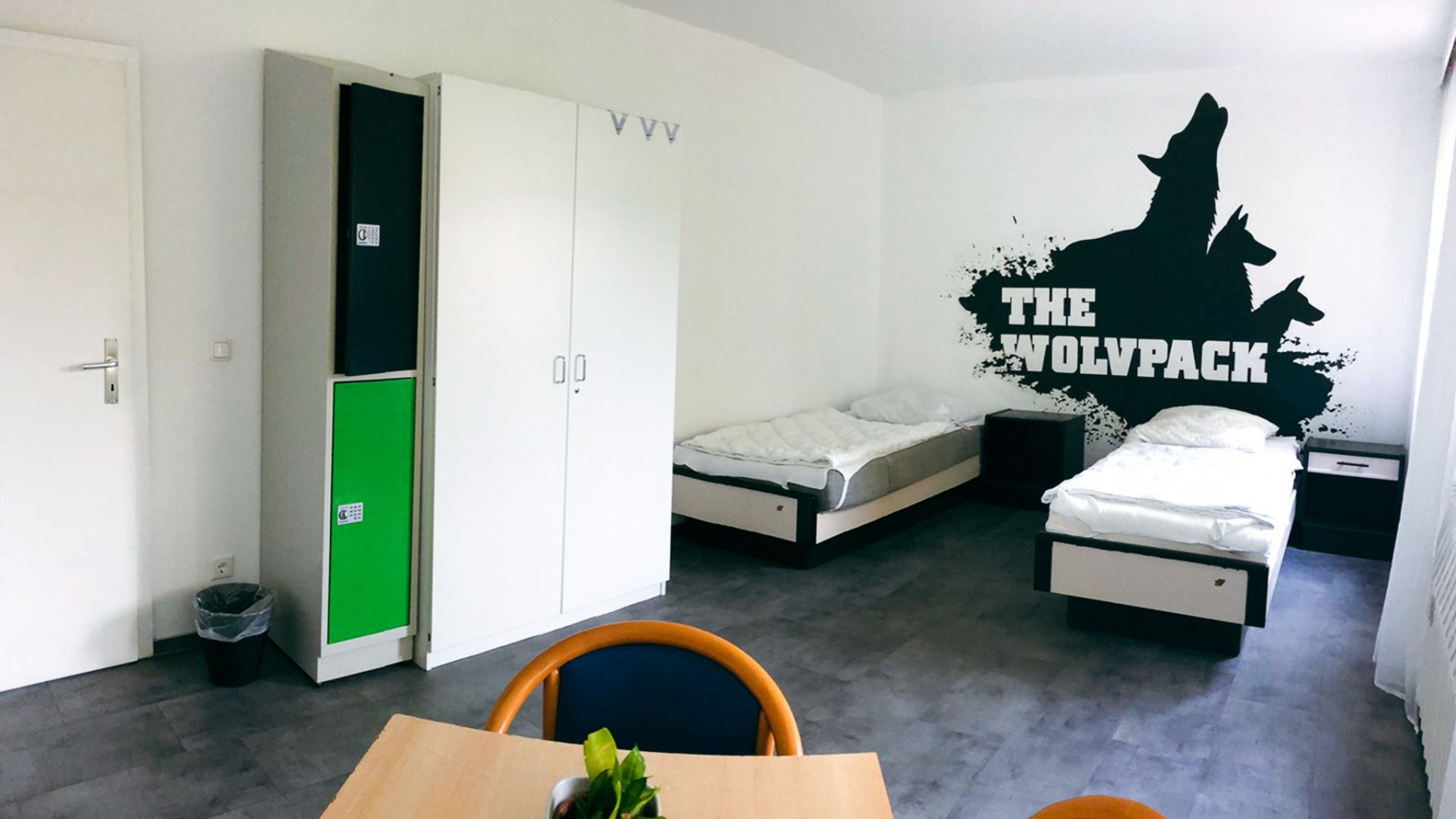Modern eingerichtetes Mehrbettzimmer im Sportcampus Schlotheim mit Einzelbetten, Spinden und Wandmotiv 'The Wolfpack'