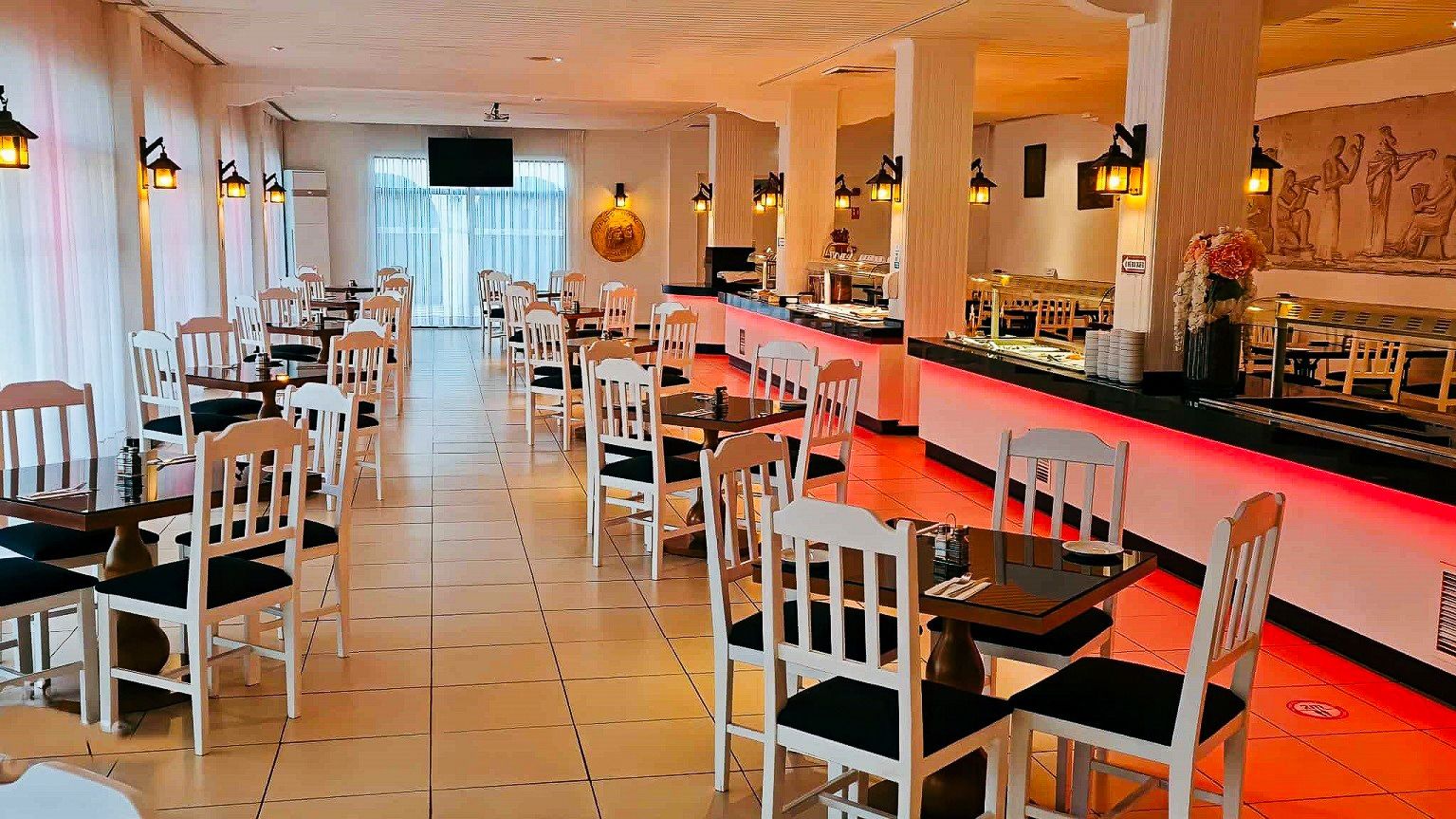 Modernes Restaurant im Sveltos Hotel mit Buffetbereich, weißen Stühlen, gedeckten Tischen und stimmungsvoller Beleuchtung.