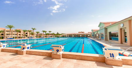 Aqua Vista Resort offers multiple outdoor pools, sun loungers, and umbrellas beneath clear blue skies&mdash;perfect for ein erfolgreiches Trainingslager in den Wintermonaten&mdash;with buildings and the sea in the background.
