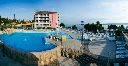Au&szlig;enansicht des Hotels Aquapark Zusterna mit rosa Fassade, Balkonen und der slowenischen Flagge.
