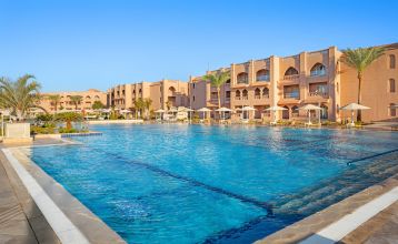Aqua Vista Resort offers multiple outdoor pools, sun loungers, and umbrellas beneath clear blue skies—perfect for ein erfolgreiches Trainingslager in den Wintermonaten—with buildings and the sea in the background.
