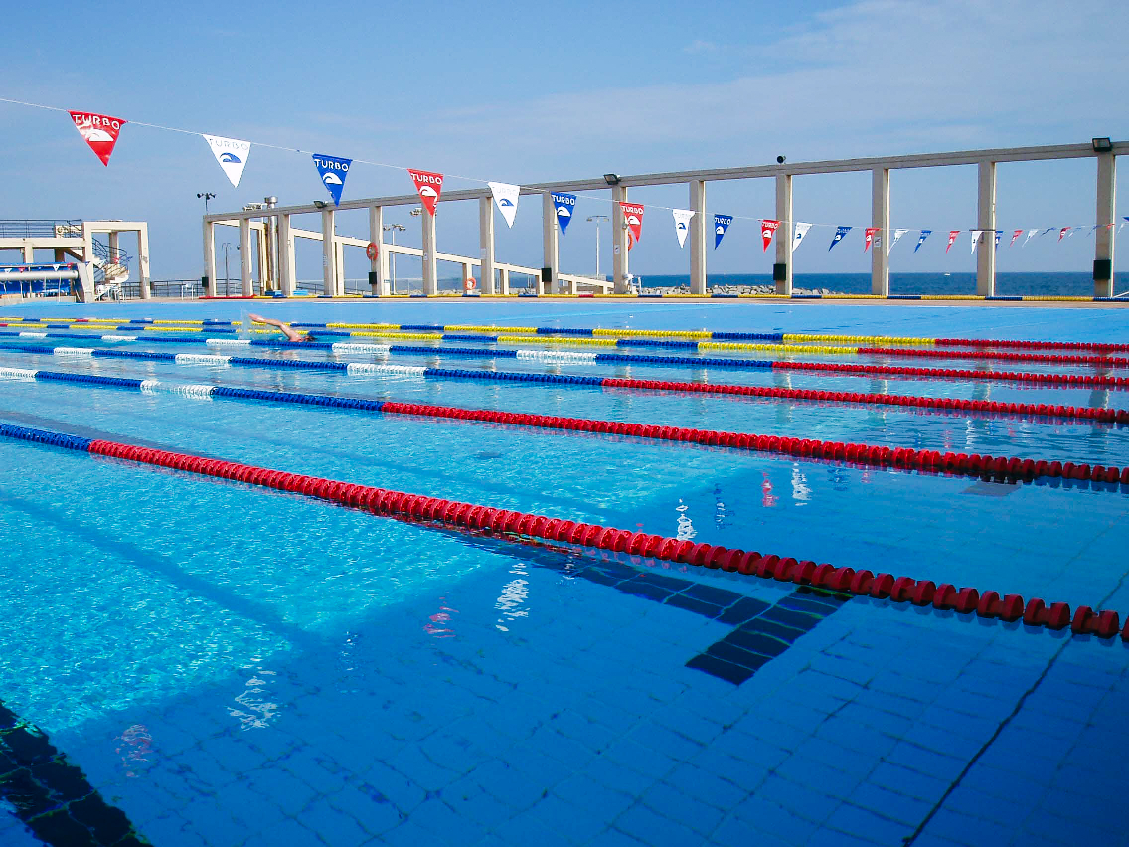 Innenansicht eines modernen Schwimmbads mit mehreren Becken, Trib&uuml;nen und Trainingsm&ouml;glichkeiten.
